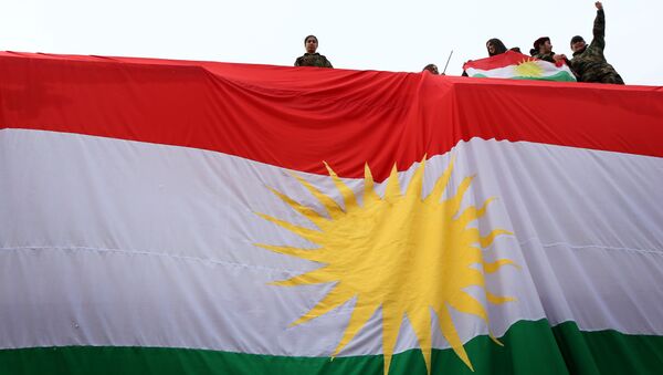 Iraqi Kurdish youths wave a national flag as they stand above a giant flag of Kurdistan during celebrations of Flag Day on December 17, 2015 - Sputnik Mundo