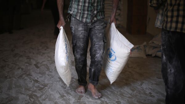 A Syrian man carries aid parcels provided by the UN World Food Programm (WFP) and the Syrian Arab Red Crescent during a food distribution by the local council in nearby areas on May 11, 2016, - Sputnik Mundo