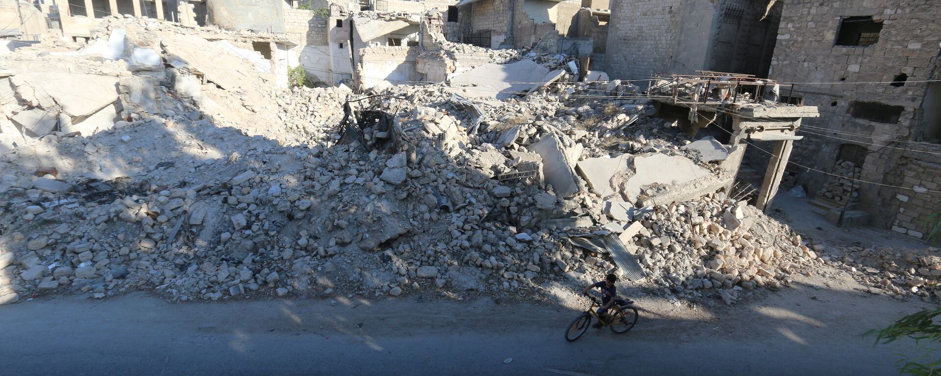 A boy rides a bicycle near rubble of damaged buildings in the rebel held al-Maadi district of Aleppo, Syria, August 31, 2016 - Sputnik Mundo, 1920, 01.06.2021
