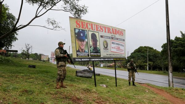 Soldiers stand guard next to a billboard showing the photographs of a police officer and a farmer, near the place where eight soldiers were killed days ago during an ambush that authorities say bore the hallmarks of the guerrilla group known as the Paraguayan People's Army in Arroyito, Paraguay, August 29, 2016. - Sputnik Mundo