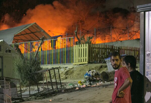 Inmigrantes observan el incendio, en el campo de refugiados de Moria, en la isla griega de Lesbos, el 19 de septiembre. - Sputnik Mundo