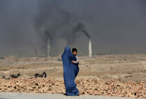 Una mujer afgana camina con su hijo cerca de una fábrica de ladrillos, en las afueras de Kabul. - Sputnik Mundo