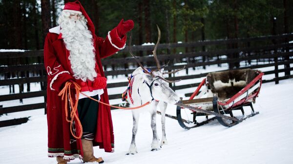 Santa Claus waves as he stands with a reindeer and sled outside Rovaniemi, Finnish Lapland on December 15, 2011 - Sputnik Mundo