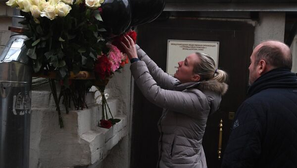 Una mujer deposita flores frente a la sede de la fundación benéfica Ayuda Justa - Sputnik Mundo