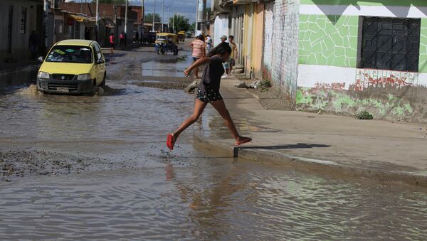 A woman cross a flooded street damaged after heavy rain in El Indio district of Piura, northern Peru - Sputnik Mundo