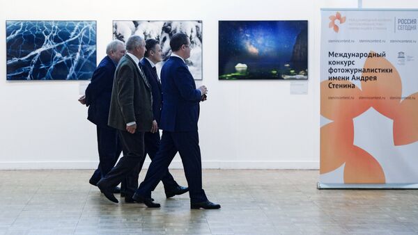 Los visitantes de la exhibición fotográfica pasan por el cartel del concurso de Andréi Stenin - Sputnik Mundo
