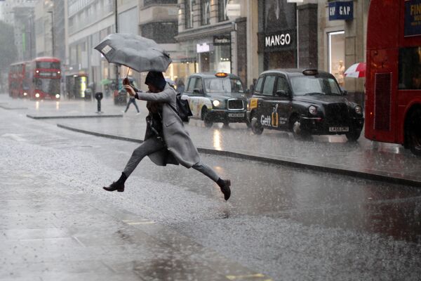Una mujer salta sobre un charco en Londres - Sputnik Mundo
