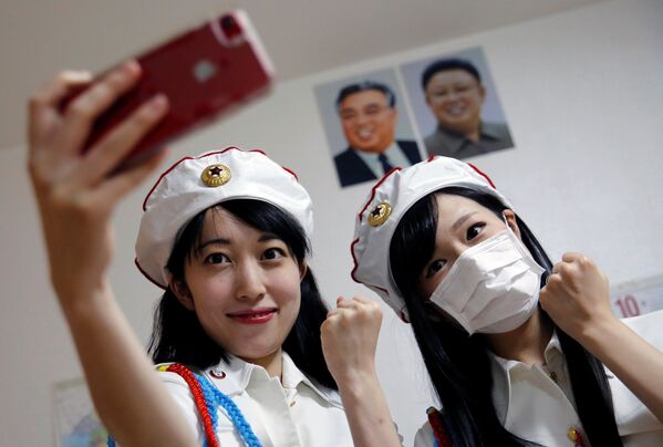 Chunhun (a la izquierda), la líder del club de fanes 'Sengun-joshi' ('Chicas militares ante todo'), posando para un selfi con una compañera y con los retratos del fundador de la RPDC, Kim Il-sung, y del segundo líder del país, Kim Jong-il. - Sputnik Mundo