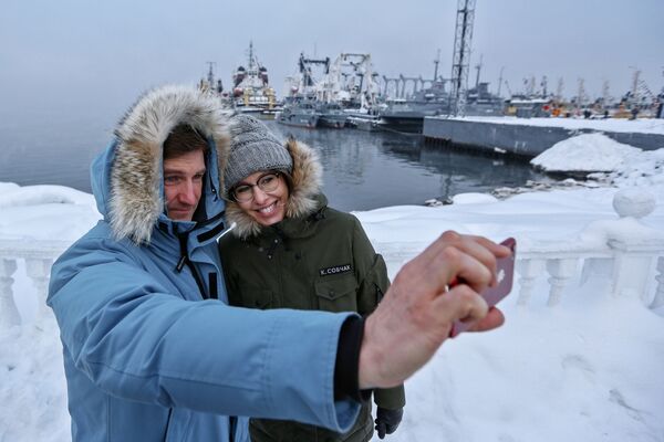 La presentadora de televisión y candidata presidencial por el partido Iniciativa Civil, Ksenia Sobchak, y un miembro de su equipo de campaña, Antón Krasovski, se toman una foto frente a unas naves en la ciudad de Severomorsk, en la región de Múrmansk - Sputnik Mundo