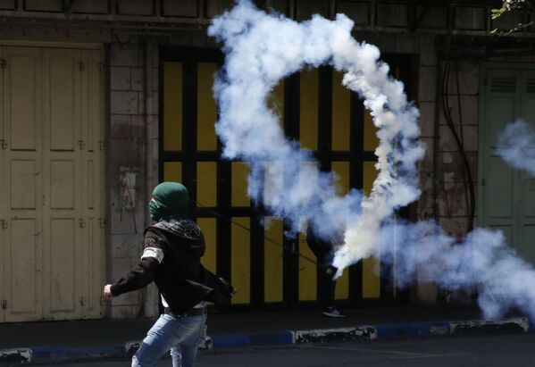 Un manifestante palestino arroja un bote de gas lacrimógeno a los soldados israelíes durante los enfrentamientos en Hebrón. - Sputnik Mundo