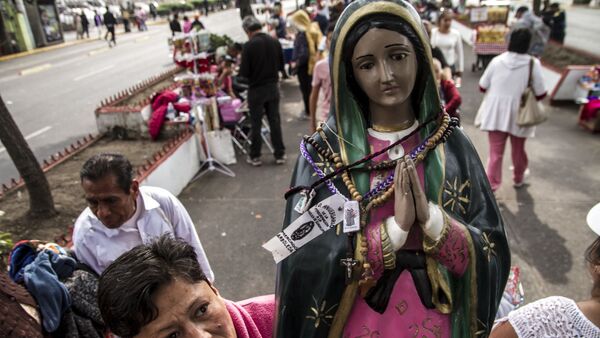 Mujer camina con una estatua de la Virgen de Guadalupe - Sputnik Mundo