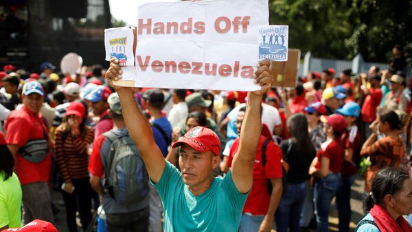 Un partidario de Nicolás Maduro con la pancarta Manos fuera de Venezuela - Sputnik Mundo