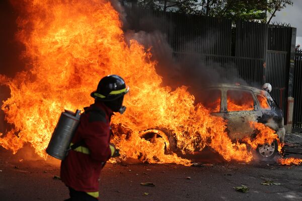 Un bombero apaga el fuego de un carro en llamas durante las protestas en Caracas - Sputnik Mundo