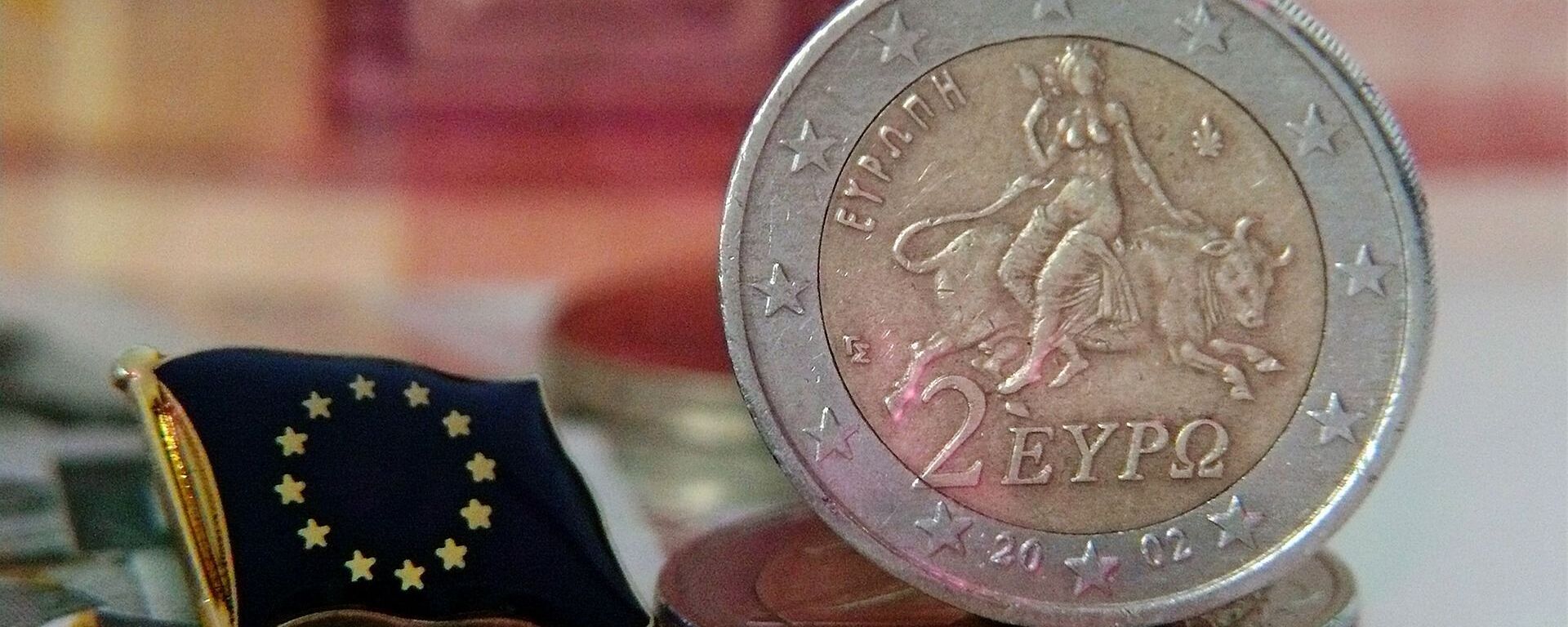 Una moneda de euro y la bandera de la UE - Sputnik Mundo, 1920, 27.12.2021