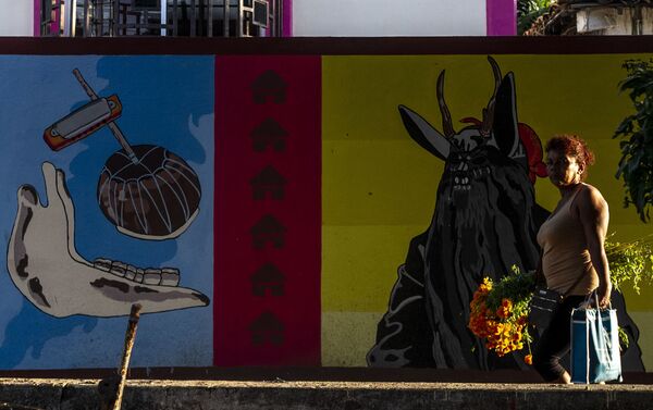 Pobladora camina durante el Día de Muertos frente a un mural referente la danza de los diablos - Sputnik Mundo