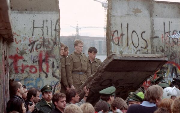 Guardias fronterizos de Alemania Oriental aparecen tras el muro de Berlín después que los manifestantes derribaron un segmento  - Sputnik Mundo