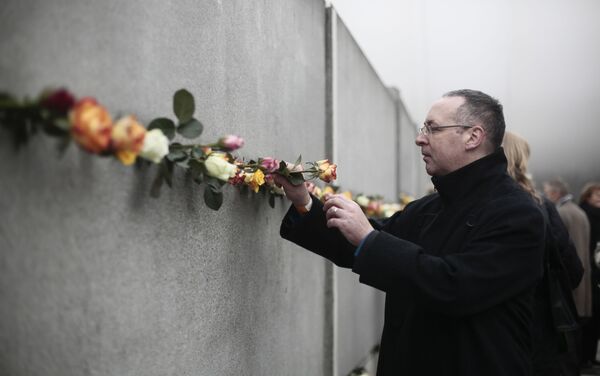 Un hombre coloca una flor en una grieta del antiguo Muro de Berlín para conmemorar a las víctimas del muro en 2014 - Sputnik Mundo