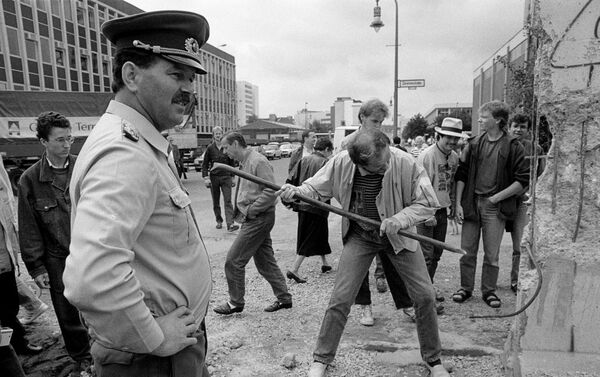 Policía fronterizo de Alemania Oriental observa a un hombre martillando una sección del Muro de Berlín en 1989 - Sputnik Mundo