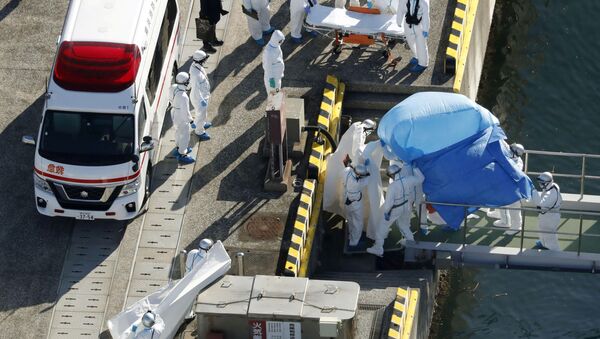 Сотрудники полиции в защитных костюмах помещают в машину скорой помощи заболевшего пассажира круизного лайнера Diamond Princes, помещенного в карантин у японского порта Йокогама - Sputnik Mundo