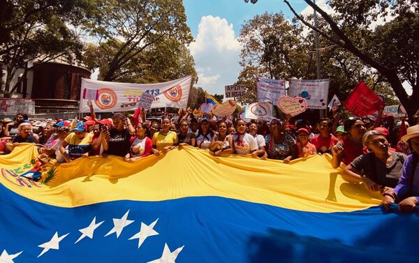 Un grupo de mujeres que participan en la multitudinaria marcha por el Dia de la Mujer en Caracas portan una bandera gigante de Venezuela mientras avanzan caminando por la avenida Universidad en direccion al Panteon Nacional, punto final de la manifestacion. Las mujeres van cantando consignas revolucionarias y en pro de los derechos de la mujer en el mundo. - Sputnik Mundo