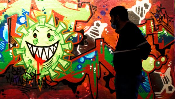 Un hombre con una mascarilla pasa al lado de un muro con un grafiti del coronavirus en el centro de Londres - Sputnik Mundo