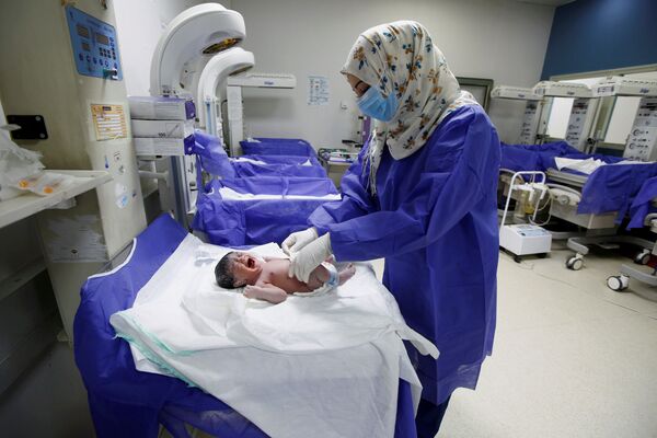 Медсестра в защитной маске и перчатках ухаживает за новорожденным в роддоме в Наджафе, Ирак - Sputnik Mundo