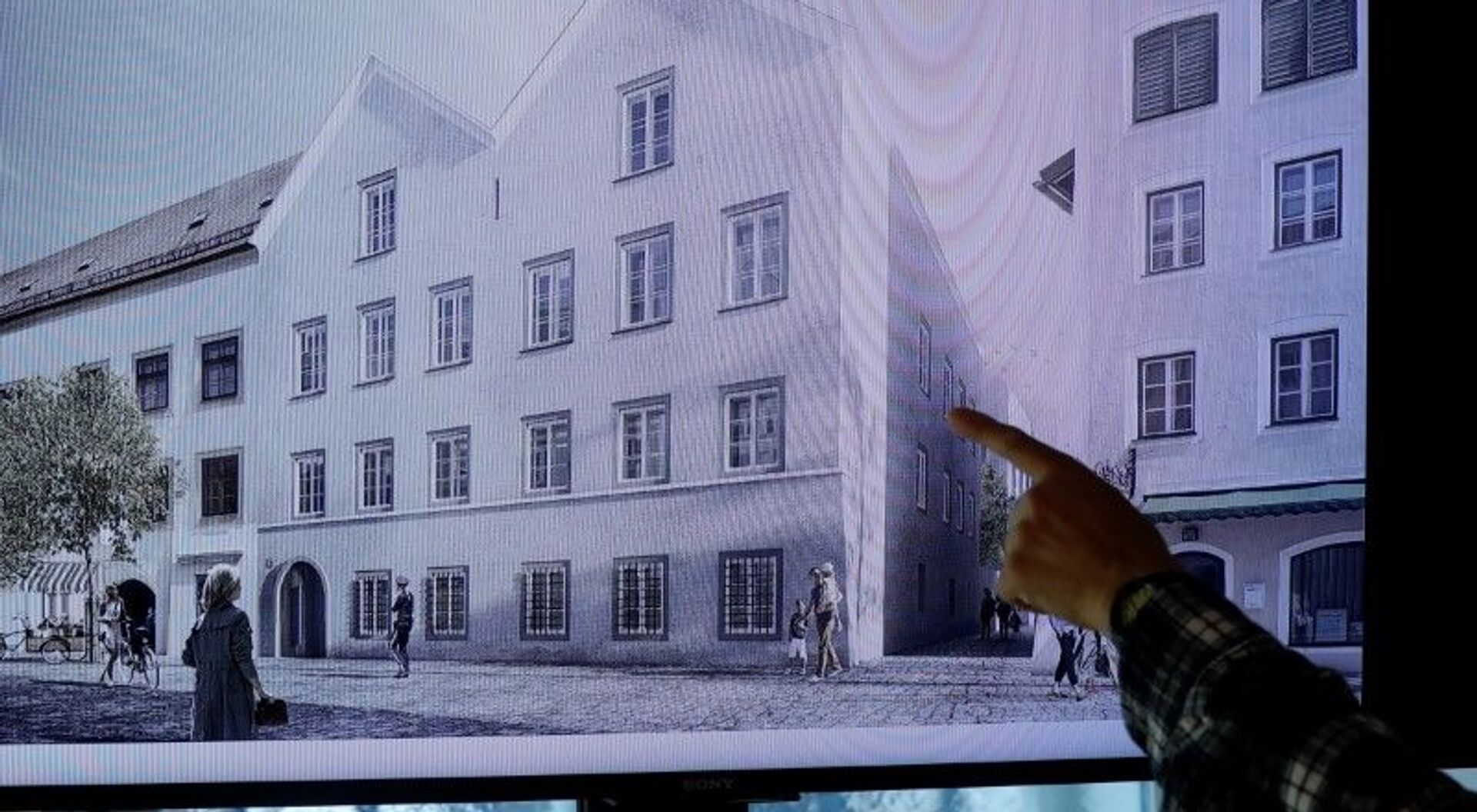 Un hombre apunta a una pantalla de televisión que muestra el plan elegido para un rediseño arquitectónico de la casa en la que nació Adolf Hitler. - Sputnik Mundo, 1920, 03.06.2020